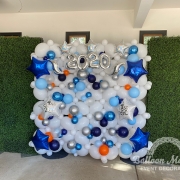 a white balloon wall in between two grass walls with blue, orange, silver, and clear small balloons, blue and silver star balloons and text that says "~2020~".