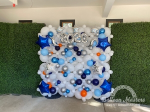 a white balloon wall in between two grass walls with blue, orange, silver, and clear small balloons, blue and silver star balloons and text that says "~2020~".