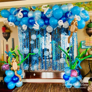 An under the sea themed balloon display hung above a doorway made of assorted blue balloons, blue tinsel, green long balloons and otter balloon animals.