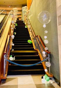 Two railings up a staircase are filled by clear, white, green, and black bubble balloons.
