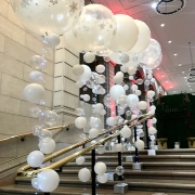 A railing up a staircase filled by pearl white and snoflake bubble balloons.