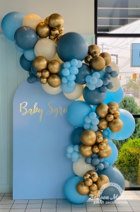 Blue, gold, cream, and dusty blue balloons arched around blue backround