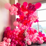 variety of pink balloons and flowers cascading up wall in display