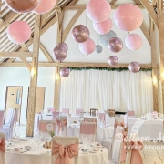 Pink and rose gold balloons individually hung from ceiling above circular tables.