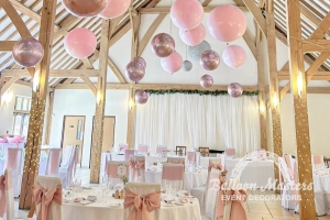 Pink and rose gold balloons individually hung from ceiling above circular tables.