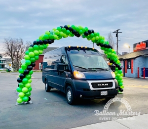 A green and black balloon arch above a ram van.