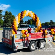 A maroon, yellow, and white balloon arch on the back of a parade trailer.
