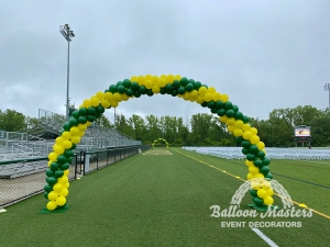 two green and yellow balloon arches at either end of the sidelines of a football field.