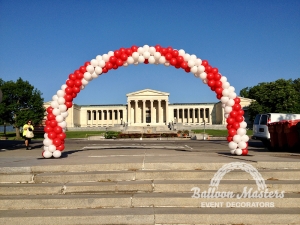 a white and red balloon arch in front of a memorial building.