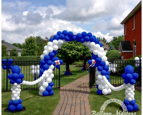A blue and white balloon arch over a fence gate walkway that is strung to a blue and white column on either side.
