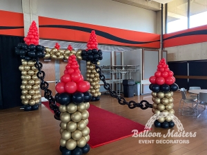 Gold, black and red balloons arranged in columns and chains creating a castle drawbridge.