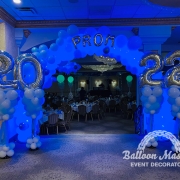 A white cloud-like balloon arch glowing with blue led lights above doorway with a balloon bouquet of "20" on one side and one of "23" on the other side.