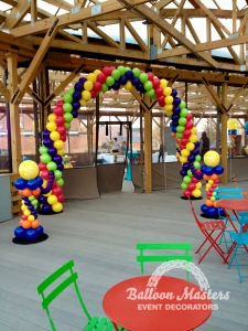 A rainbow balloon arch over a walkway that is strung to a rainbow column on either side.