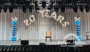 the words "20 years" arched over a stage with silver and blue arches with star balloons at top at either side of stage