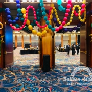 Marti Gras balloon display with wildly strung balloon garlands hung above doorway and two balloon columns on either side of doorway.