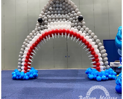 gray white and red balloon arch, shaped to resemble shark head.