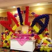 A yellow, red and purple balloon display with the text "MILA" made of balloons overtop.