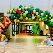A green and brown tree balloon arch with little pink flower balloons and forest animals scattered throughout. The words "SHA" are showcased at the side.