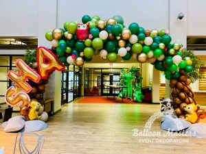 A green and brown tree balloon arch with little pink flower balloons and forest animals scattered throughout. The words "SHA" are showcased at the side.