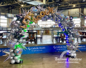 A 70s themed balloon arch covered in silver balloons, silver stars, and disco balls.