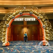A large, gold, white and orange balloon arch with Michael Kors logos evenly spaced on it.