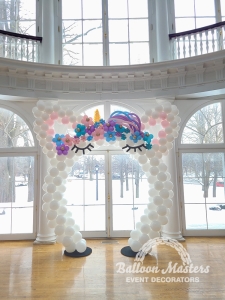 a white balloon arch shaped to look like a unicorn with a gold horn and pink, purple, and blue hair.