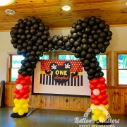 A yellow, red and black balloon arch shaped to look like mickey mouse.