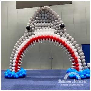 gray white and red balloon arch, shaped to resemble shark head.