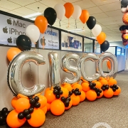 silver lettering balloons that spell "cisco" surrounded by orange and black clusters with orange, black, and white singular balloons arranged in arch formation.