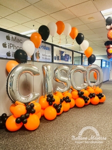 silver lettering balloons that spell "cisco" surrounded by orange and black clusters with orange, black, and white singular balloons arranged in arch formation.
