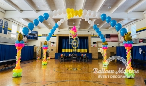 four pink, orange, yellow and green balloon columns with smiling sun balloons at top and two arch formations attached to columns creating a cross formation.