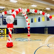 red, white and snowflake clear singular balloons arranged in two arch formations that overlap creating a cross shape. Each end attached to a red and whit column.
