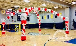 red, white and snowflake clear singular balloons arranged in two arch formations that overlap creating a cross shape. Each end attached to a red and whit column.