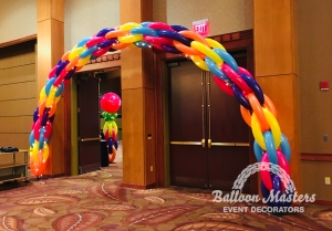 A blue, purple, blue, orange and yellow balloon arch.