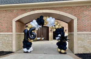 black, gold, and white balloon arch with black and silver star attachments with "16" attached.